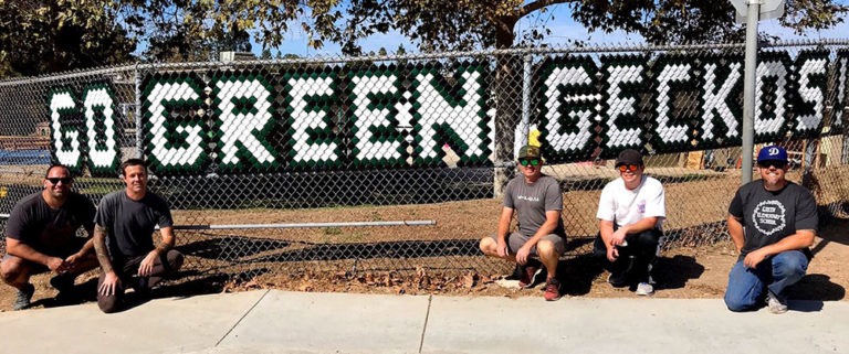 Volunteers beside a fence displaying Go Green Geckos signage