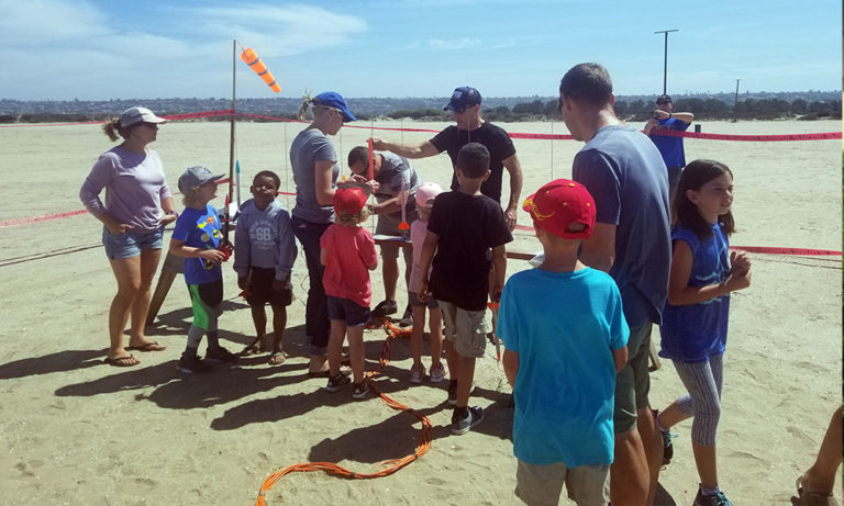 Children and adults gather around model rockets on a school field